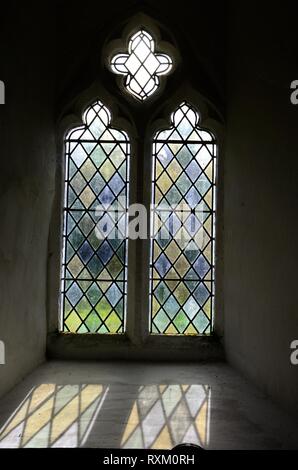 Luce che risplende attraverso una finestra di vetro colorato a St Odoceus Chiesa Llandawke Laugharne ora nella cura degli amici di Chiese Friendless Galles Foto Stock