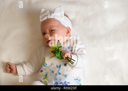 Bellissima bambina tenendo un fiore su coltre bianca Foto Stock