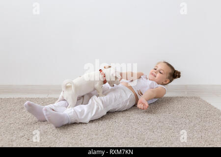 Il Pet proprietario, bambini e cani concetto - bambina sdraiato sul pavimento con grazioso cucciolo e riproduzione Foto Stock