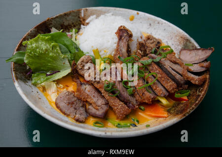 Chiudere la porzione di fettine arrostito croccante anatra alla pechinese curry con riso e insalata sulla piastra sopra il tavolo, ad alto angolo di visione Foto Stock