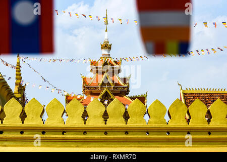 (Fuoco selettivo) Splendida vista della bellissima Wat That Luang Neua con alcuni sfocato Laos bandiere sventolano in primo piano. Foto Stock