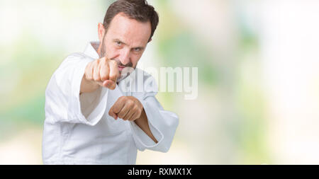 Bella la mezza età senior uomo indossare il kimono uniforme su sfondo isolato il pugno di punzonatura per combattere, aggressivo e arrabbiato attacco, minaccia e violenc Foto Stock