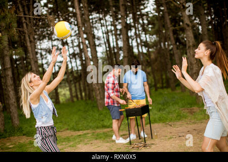 Giovani donne giocando a pallavolo su picnik in primavera la natura mentre gli uomini preparare grill Foto Stock