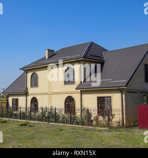 Casa del mattone giallo e marrone e tetto ondulato in metallo. Tralicci su windows Foto Stock