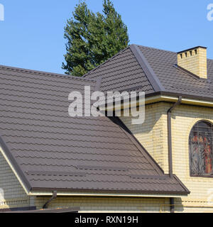 Casa del mattone giallo e marrone e tetto ondulato in metallo. Tralicci su windows Foto Stock