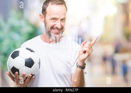 La mezza età annoso senior man holding soccer football palla su sfondo isolato molto felice rivolto con la mano e le dita per lato Foto Stock