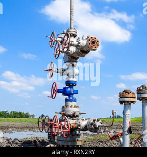 Olio bene dopo la riparazione nel fango e pozzanghere. Olio e apparecchiature di testa del pozzo. La valvola manuale con volantino di manovra di apertura e chiusura della linea di flusso Foto Stock