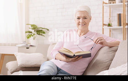 Senior sorridente donna libro di lettura a casa Foto Stock