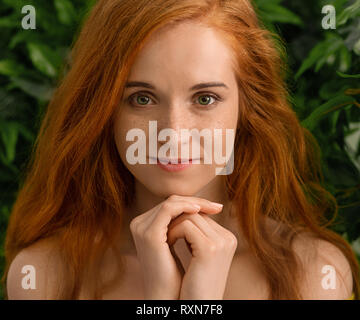 Giovane ragazza redhead guardando la telecamera, foglie verdi sullo sfondo Foto Stock