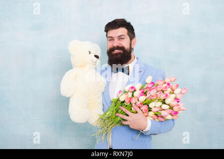 Uomo Barbuto gentleman suit bow tie tenere orsacchiotto di peluche e bouquet. Felice e nell'amore. Gentleman rendendo sorpresa romantica per lei. Gentleman regalo romantico. Auguri di compleanno. Buon compleanno il mio amore. Foto Stock