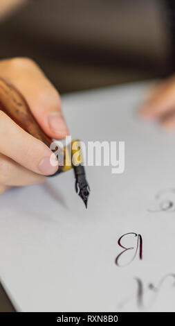 Calligrapher mani scrive una frase sul libro bianco. Inscrivendo ornamentali in lettere decorate. La calligrafia, graphic design, scritte, la grafia Foto Stock