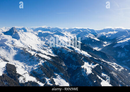 Luminoso panorama delle gamme della montagna con la neve e il ghiaccio sulle cime contro il cielo blu in inverno e fitte foreste presso la base della montagna. Foto Stock