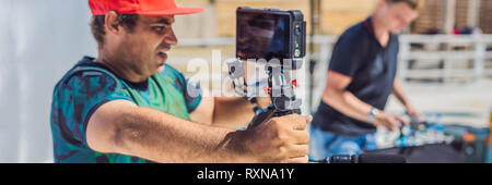 Il team di produzione su un commerciale riprese video. Steadicam operatore utilizza il a 3 assi fotocamera stabilizzatore e cinema-grade fotocamera. BANNER, formato lungo Foto Stock