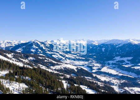 Vista da un drone su un inverno montagne coperte di foreste e di neve nelle Alpi e piccoli villaggi in distanza. Foto Stock