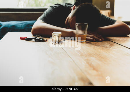 Uomo ubriaco che dorme sul tavolo con le pillole e un bicchiere di whiskey e le chiavi dell'auto. Foto Stock