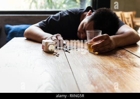 Ubriaco uomo con un bicchiere di whiskey e chiave auto dormire sul tavolo con le pillole. Foto Stock