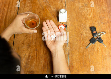 Uomo con pillole e bicchiere di alcool con le chiavi dell'auto sul tavolo di legno. Foto Stock