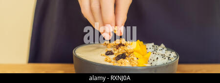 Donna frullato di cuochi bocce fatta con mango, banana, granola, cocco grattugiato, dragon frutta, semi di Chia e menta su sfondo di legno. Concetto di frutta Foto Stock