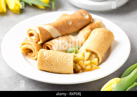 Frittelle di sottile (crepes) con ripieno di mele, rotoli farciti, Russo del cibo tradizionale per maslenitsa, francese dessert, prima colazione con i tulipani sulla madre d Foto Stock