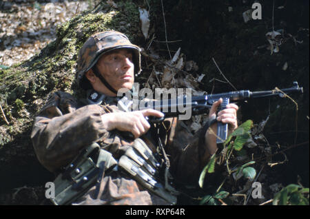 A WW2 Reenactor tedesco indossa il periodo uniforme di un Tedesco Waffen SS Soldier tenendo un MP40 pistola automatica Foto Stock