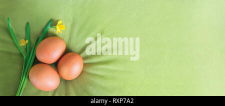 Arancione tre uova di Pasqua e narcisi su un velluto, oliva, canvas verde dello sfondo. Concetto di biglietto di auguri, promozione, poster, volantini, banner web Foto Stock