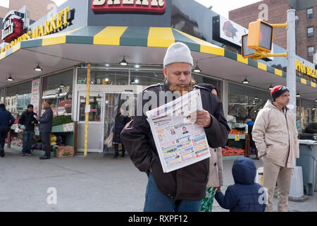 Un uomo musulmano con un henné barba tinto legge un giornale bengalesi sulla 37th Avenue a Jackson Heights, Queens, a New York City. Foto Stock