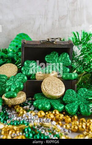 San Patrizio scrigno pieno di monete e glittery trifogli. Verde, Oro e argento perle sfocato in primo piano. Mattonelle in pietra neu Foto Stock