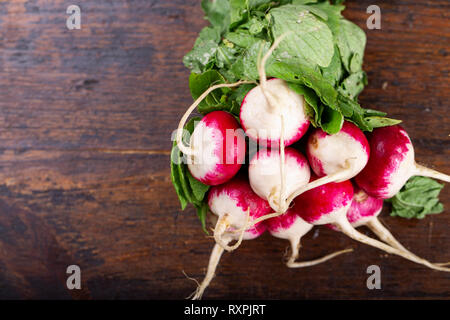 Estate raccolte di ravanello rosso. Coltivazione biologica di verdure. Grande grappolo di crudo fresco giardino succosa ravanello su schede marrone pronto a mangiare. Foto Stock