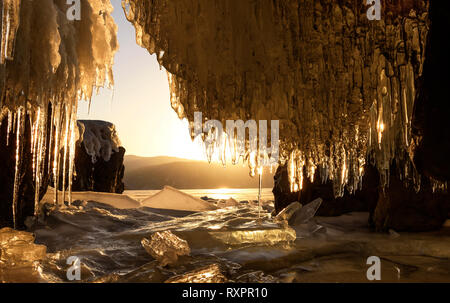 Incredibile sunrise oltre le montagne e il lago ghiacciato in inverno dalla caverna di ghiaccio con ghiaccioli. Lago Teletskoye, Altai, Russia Foto Stock