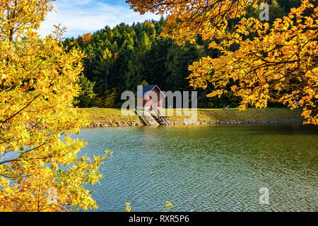 Bellissima vista della piccola casa in legno sulla riva del lago vicino Bosco in autunno Foto Stock