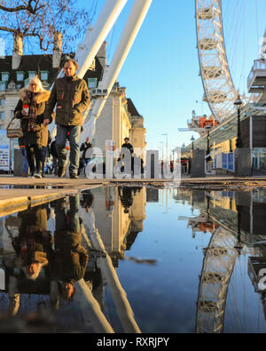 South Bank di Londra, Regno Unito. 10 mar 2019. La gente a piedi nel tardo pomeriggio di sole su Londra il South Bank. In seguito ad una giornata di sole e pioggia, il tardo pomeriggio vede un ritorno della serata calda luce solare con un sacco di pozzanghere e riflessioni vicino al London Eye. Credito: Imageplotter/Alamy Live News Foto Stock