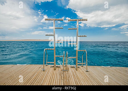 Metallo Acciaio scale sul retro pontatura in teak di un lussuoso yacht a motore vela su un oceano tropicale con sfondo con cielo nuvoloso Foto Stock