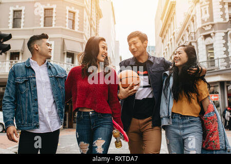 Un gruppo di uomini e donne a piedi all'aperto con lo skateboard e il basket. Due coppie camminando sulla strada della citta'. Foto Stock
