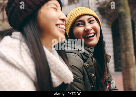 Vista laterale di due donne asiatiche in abbigliamento invernale stando all'esterno. Le donne in vestiti caldi sorridente e divertimento all'aperto. Foto Stock
