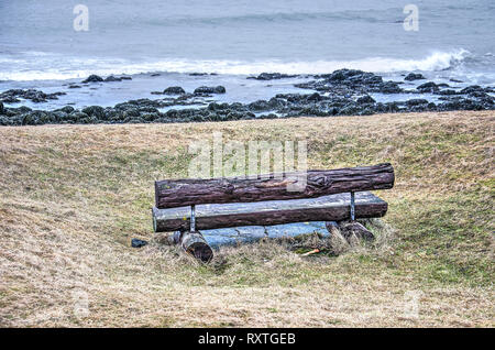 Poco fatte di tronchi di alberi collocati in erba con una vista verso una spiaggia rocciosa e l'oceano in un sobborgo di Reykjavik Foto Stock