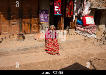Un anziana signora nepalese prende un resto da seduto su una parete. Bhaktapur, Nepal. Foto Stock