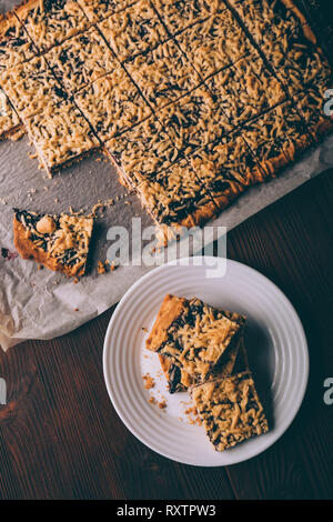 Pane appena sfornato, biscotti fatti in casa con la marmellata tagliato in quadrati sulla placca da forno e la piastra sul marrone sfondo rustico, vista dall'alto. Foto Stock