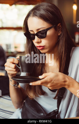 Giovane e bella ragazza beve caffè in un bar Foto Stock