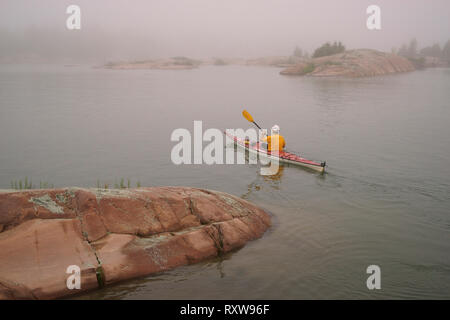 Un kayaker su una mattinata nebbiosa,lasciando per una racchetta in Phillip Edward Island area di Georgian Bay, Ontario, Canada Foto Stock