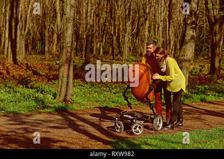 Servizio di baby sitter. Uomo Barbuto e pretty woman baby con baby pram nella primavera del parco. Servizio di custodia dei bambini per i genitori che lavorano Foto Stock