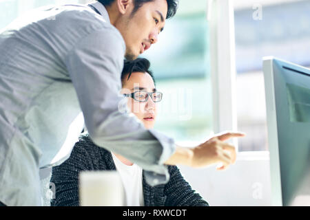 Due giovani asiatici dirigenti aziendali che lavorano insieme con computer desktop.