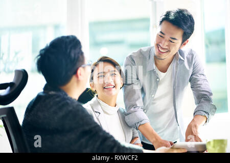 Tre giovani compagni di squadra asiatica lavorando insieme avente una piacevole discussione aziendale in ufficio. Foto Stock