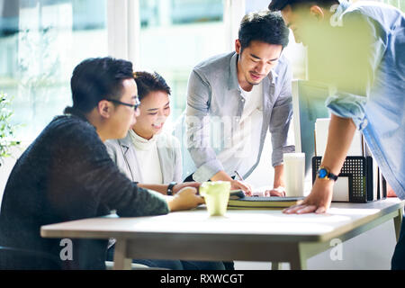 Il gruppo di quattro giovani asiatici aziendale dirigenti riuniti in office discutere di affari in ufficio. Foto Stock