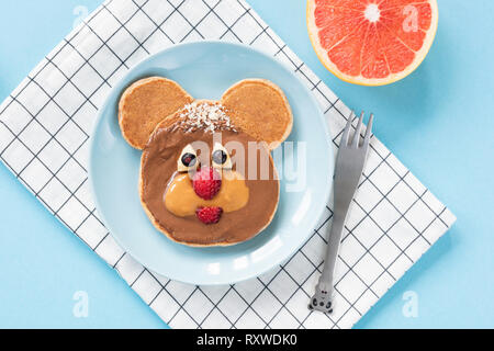 Funny Teddy Bear pancake arte cibo per bambini su un blu brillante background. Vista dall'alto. Una sana colazione pasto per bambini Foto Stock