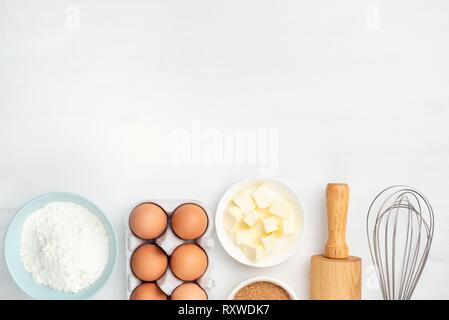 La cottura Ingredienti e utensili da cucina su sfondo bianco. Uova di gallina, burro, zucchero, farina, mattarello e baffo. Cucinare, forno, pasticceria o c Foto Stock