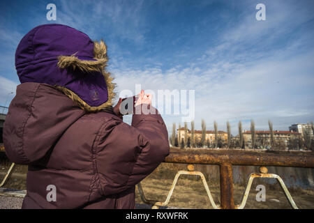 Bambino con viola giacca invernale e un cappello riprese con una videocamera esterna su un cielo blu sullo sfondo Foto Stock