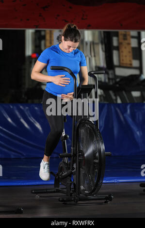 Donna incinta facendo un intenso allenamento in palestra aria bike Foto Stock