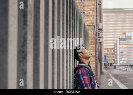 Contenuto giovane uomo asiatico appoggiato contro una parete Foto Stock