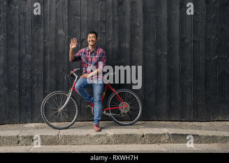 Sorridente giovane con una bicicletta salutando Foto Stock