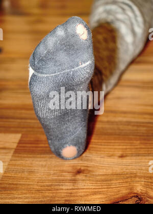 Usurati calze con fori e le dita dei piedi spuntavano di loro sul vecchio pavimento in legno Foto Stock